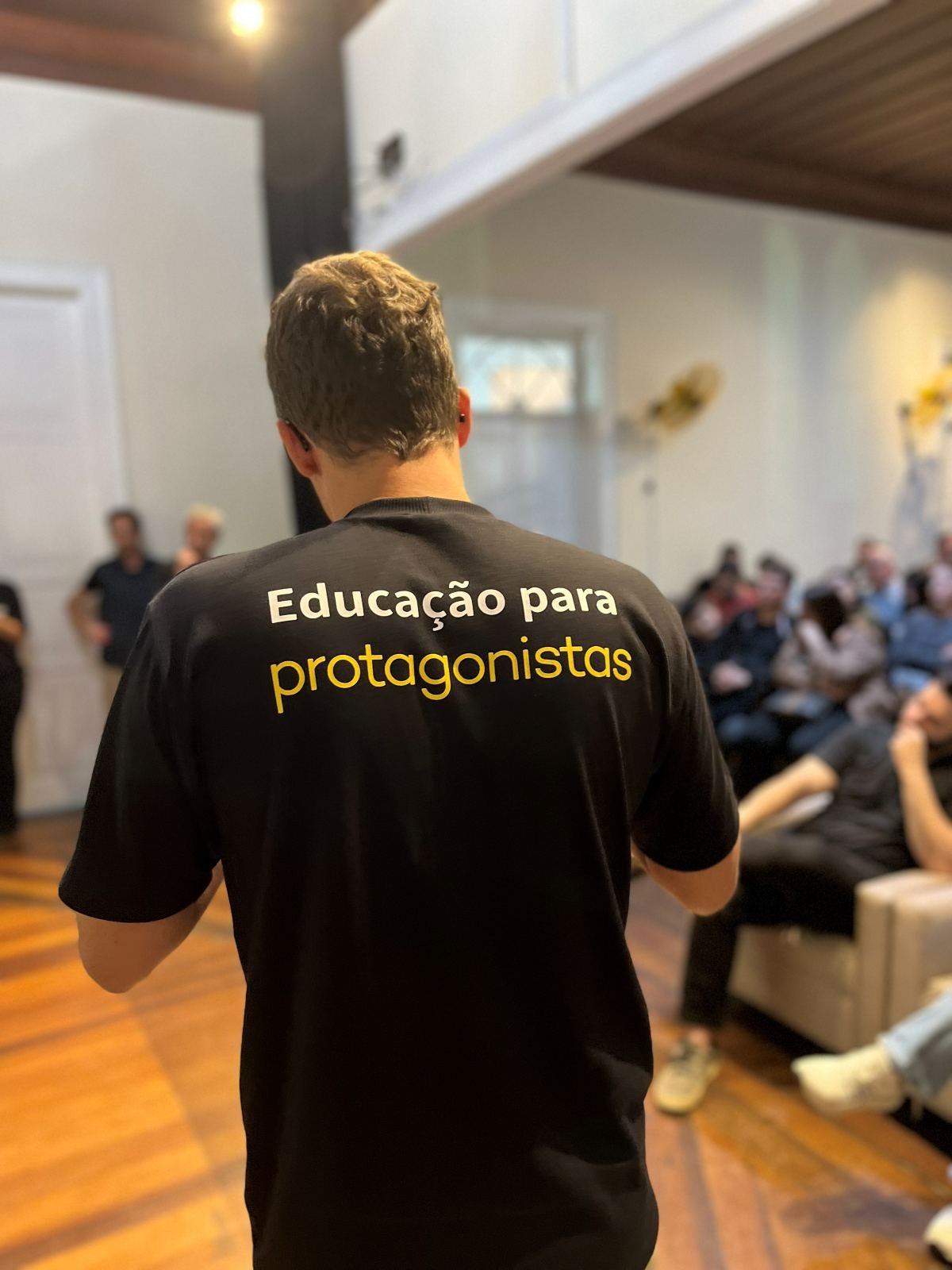 Facilitator seen from behind wearing an 'Education for protagonists' T-shirt, facing the DemoDay audience